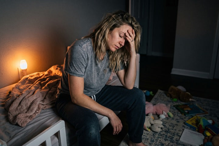 Ersch&ouml;pfte Mutter sitzt abends auf dem Bett